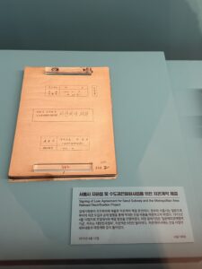 An artifact is on display under some glass with an explanatory placard under it. The paper is yellowed and looks old.