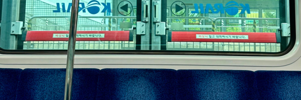 The inside of a train chair showing the top of a row of dark blue seats. Above that, outside the window, the logo for Korail is reflected.