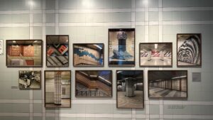 A wall mimicking the blue and white tile of a subway station displays a multitude of pictures also of various subways station tiles.