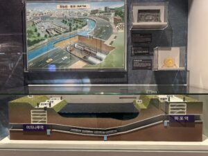 A large diorama shows a tunnel going under the Han River with a miniature subway in the tunnel directly under the water. Above the diorama is an explanatory poster of the construction method. 